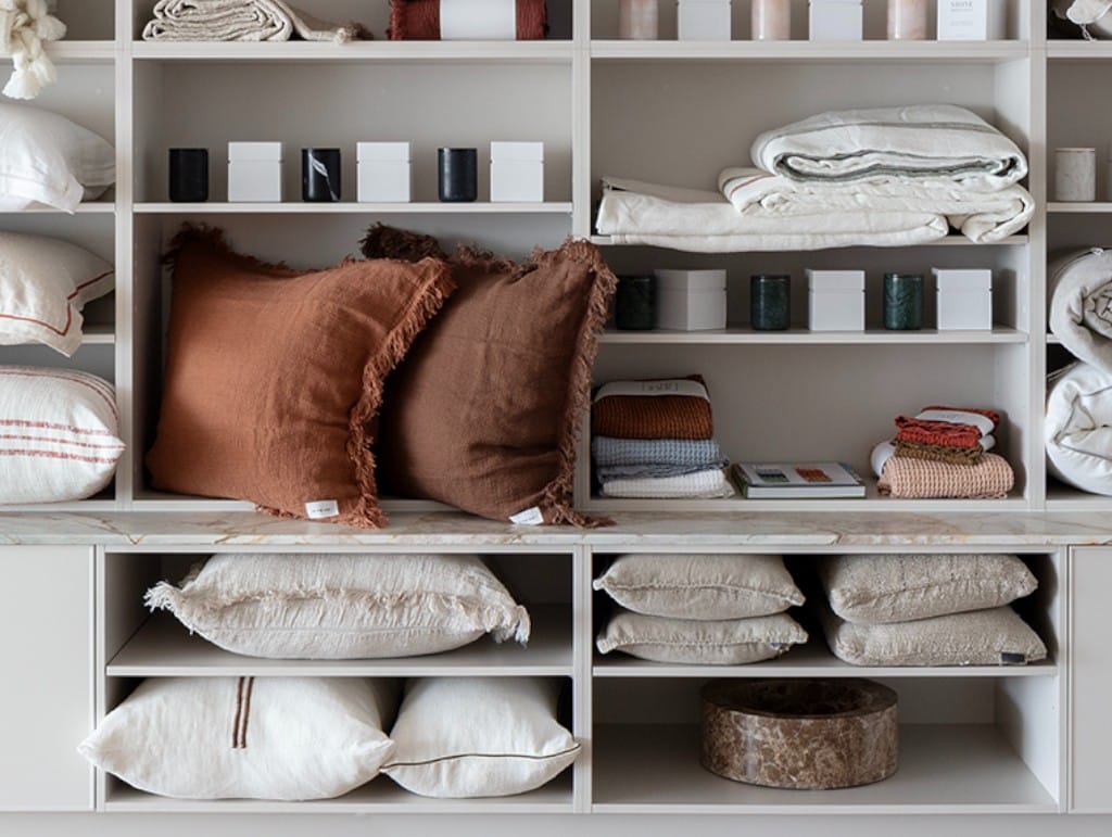 Shelf display featuring Eadie Lifestyle and In The Sac natural cotton and linen cushions, paired with handcrafted stone homewares and soft neutral textiles, styled for a relaxed, refined interior look.