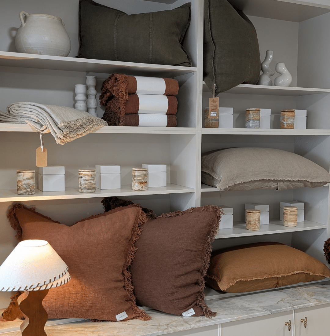 Refillable stone candle holders styled on shelving with linen cushions in a curated interior setting