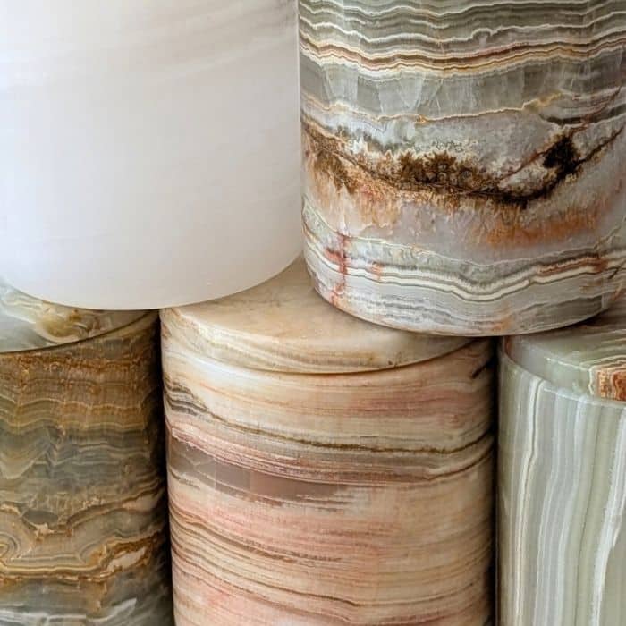 Close-up of natural onyx stone candle jars stacked together, showing unique marbled veining in white, grey and rose tones