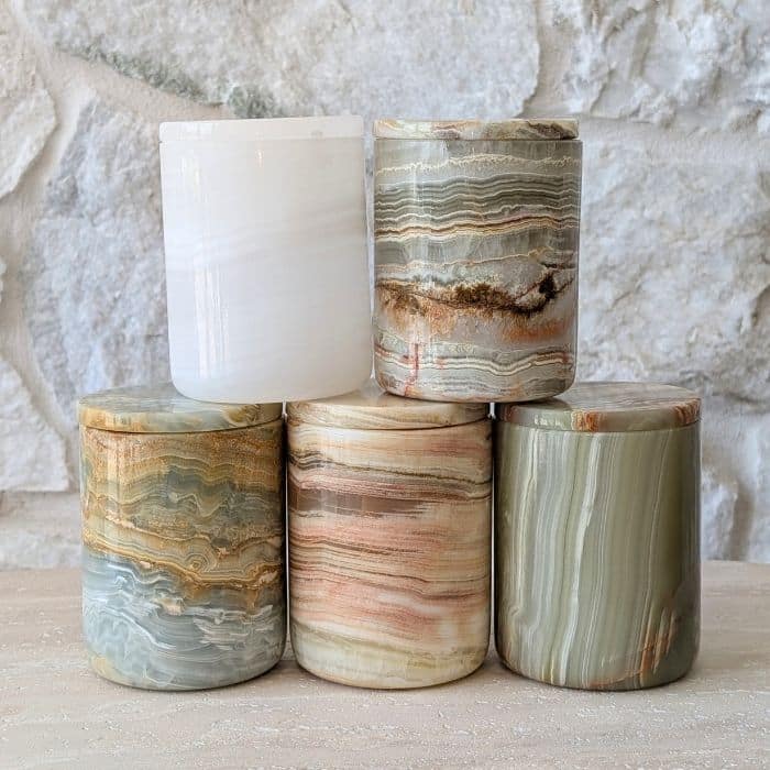 Five natural onyx stone candle jars arranged in a pyramid against a rustic stone wall