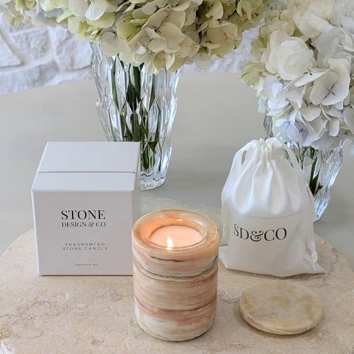 Lit Stone Design & Co fragranced stone candle beside its packaging box and SD&CO drawstring gift bag, styled with white hydrangeas